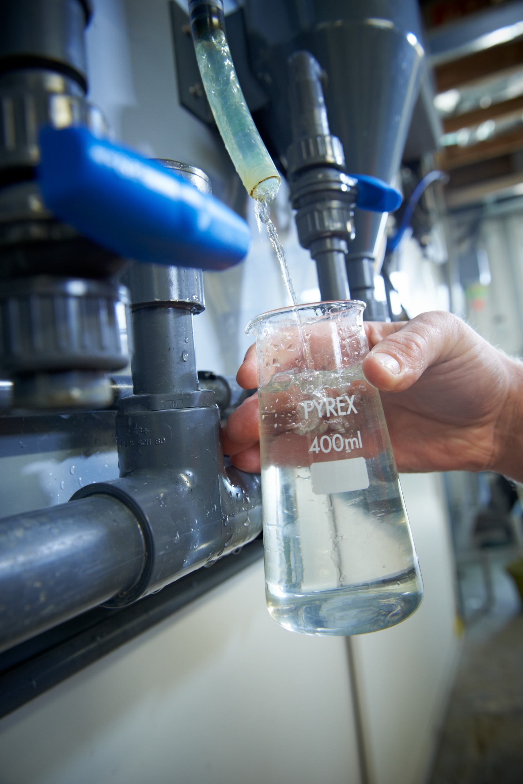 A testing glass being filled with water from a pipe in a water treatment plant.