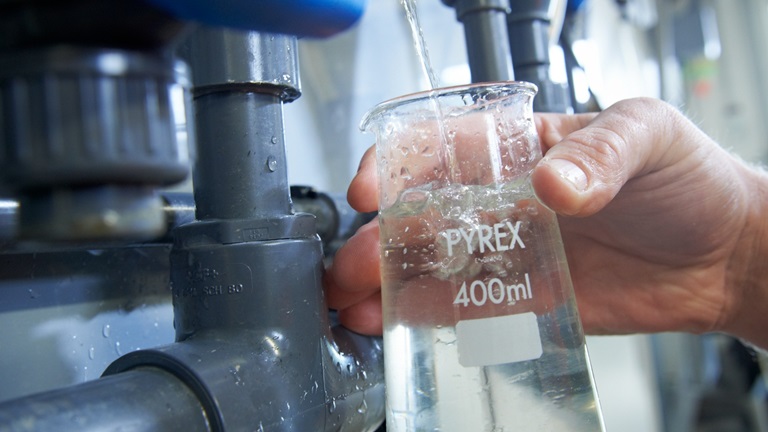 A testing glass being filled with water from a pipe in a water treatment plant.