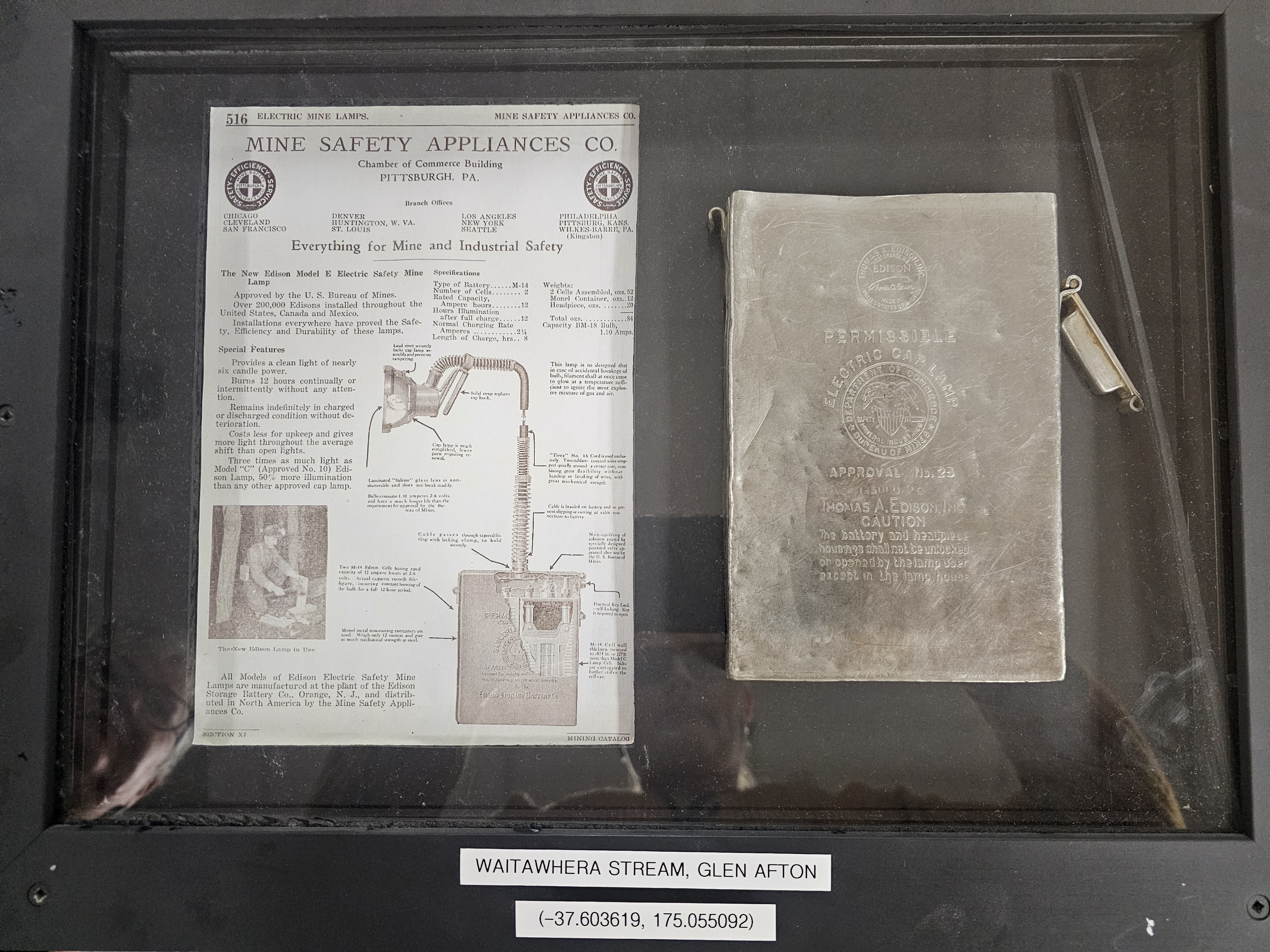 Display case featuring a vintage mine safety brochure and an Edison Electric Cap Lamp instruction booklet. Location coordinates: Waitawhera Stream, Glen Afton.