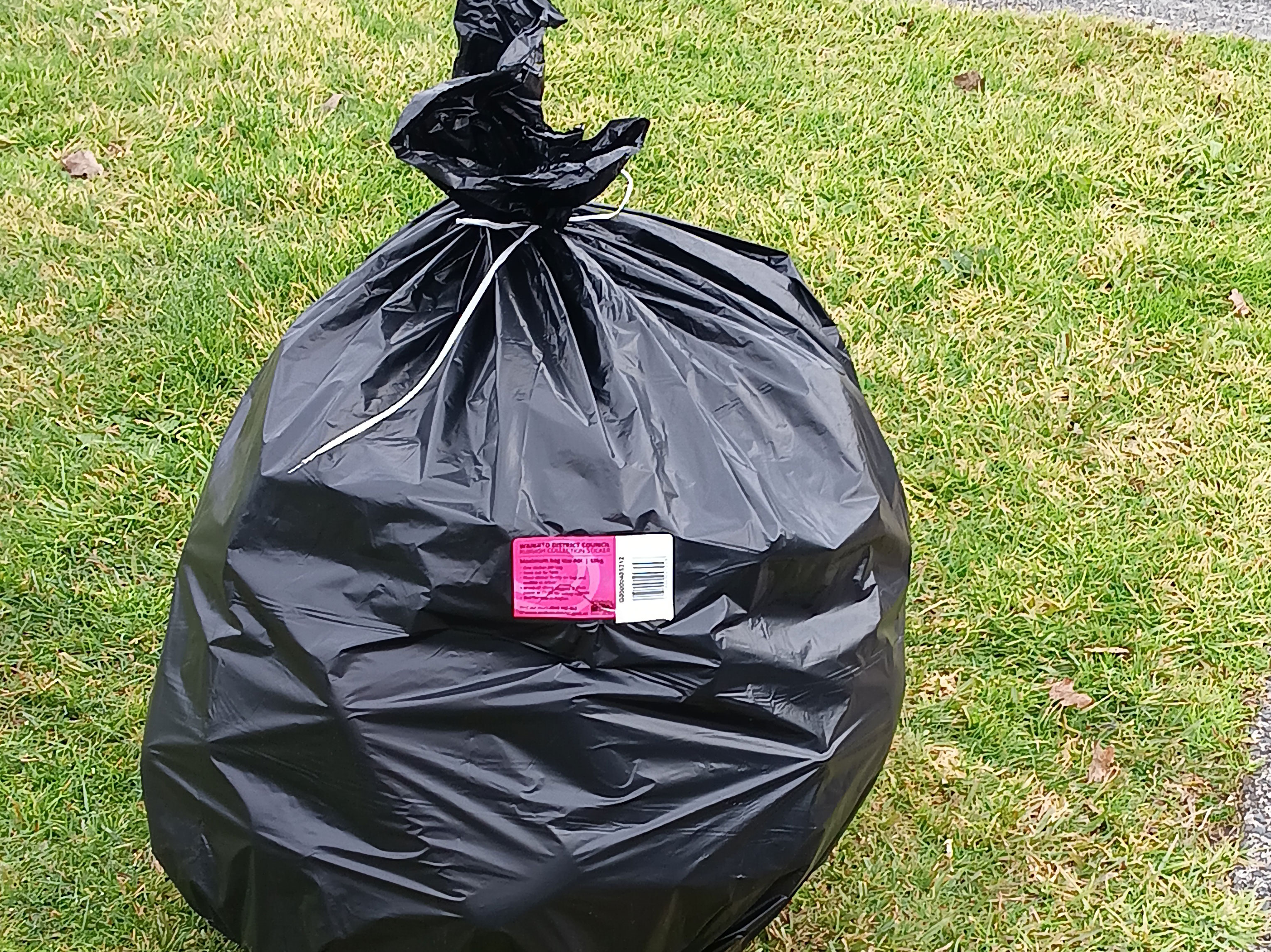 Black rubbish bag with pink council sticker on the kerb for collection